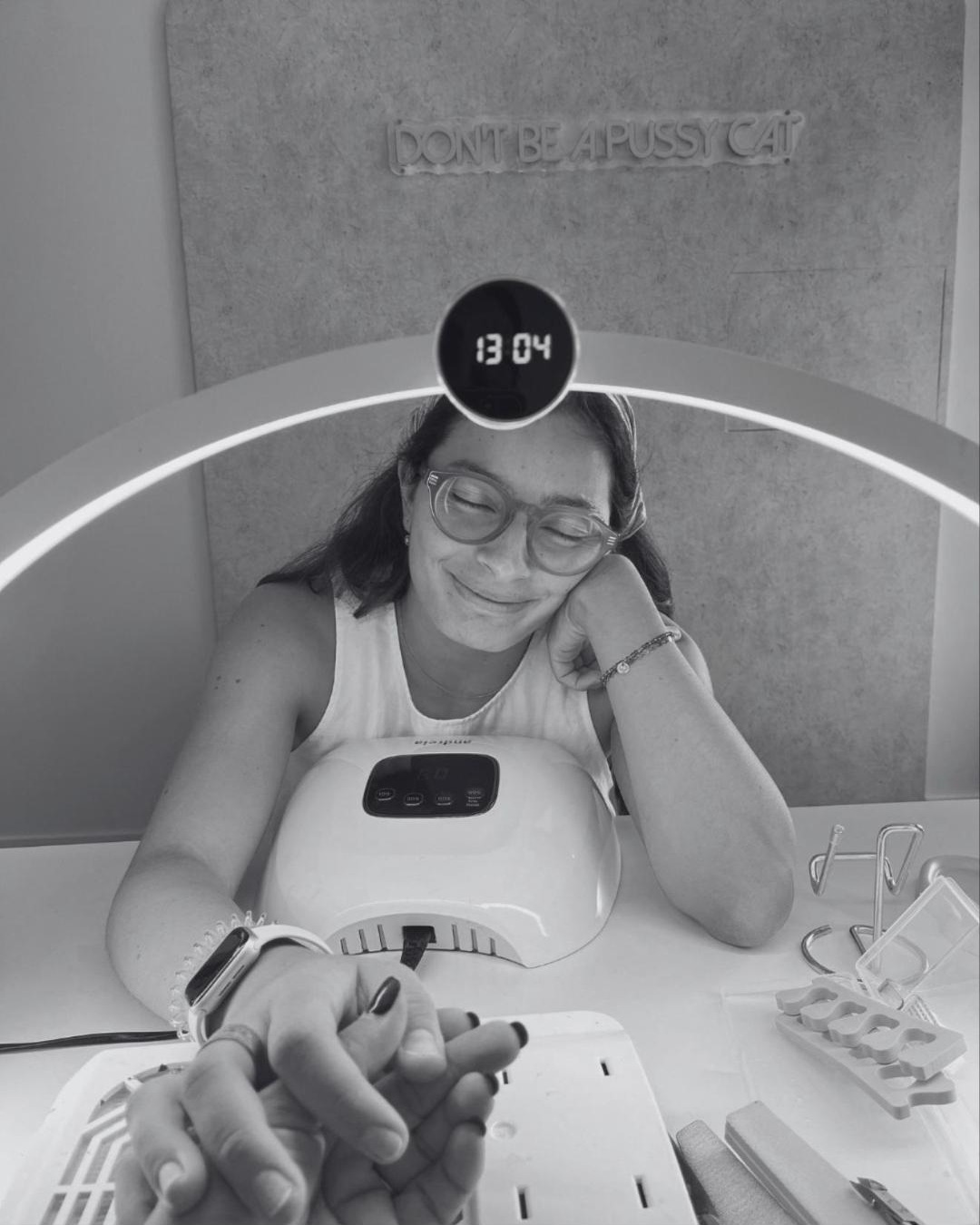 Cliente sorridente na mesa de manicure, com o néon do estúdio ao fundo