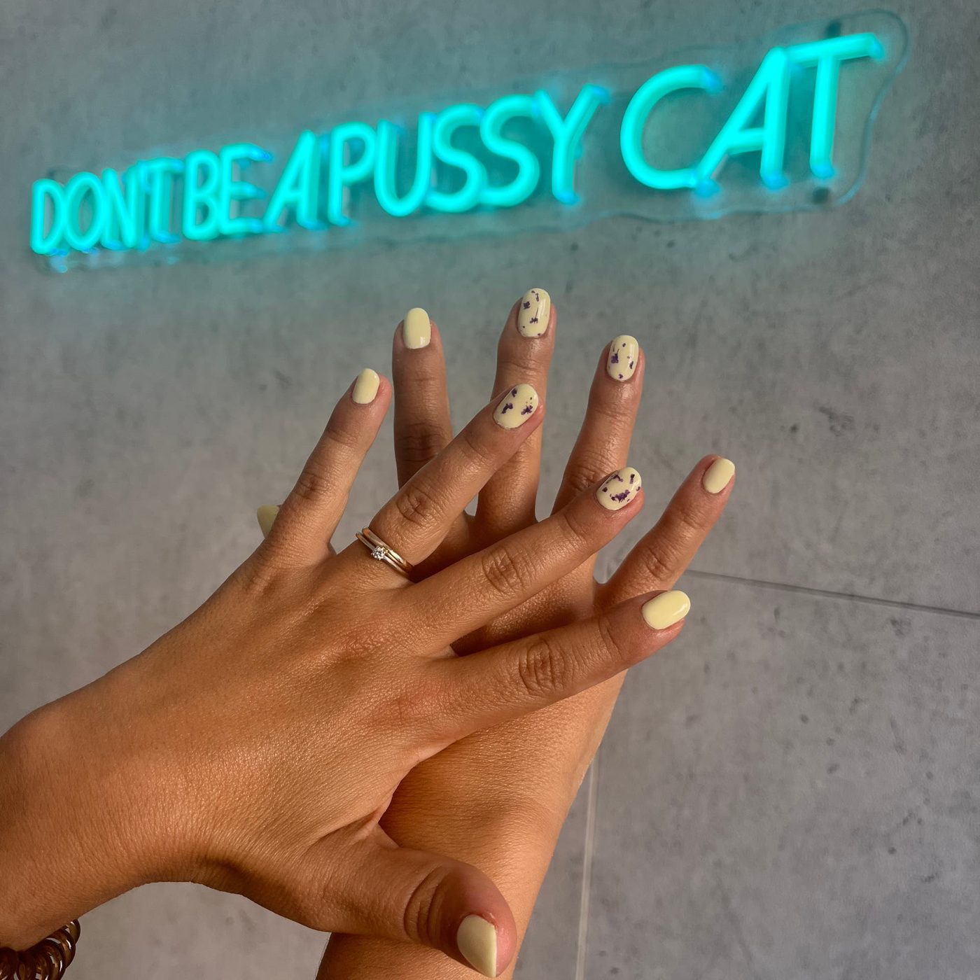 Duas mãos com nail art em frente ao néon do estúdio